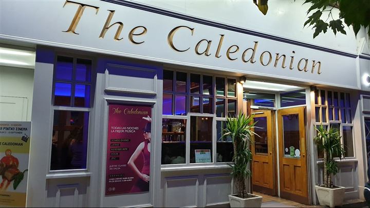 Fachada de The Caledonian de noche, con su rótulo dorado y las puertas de madera